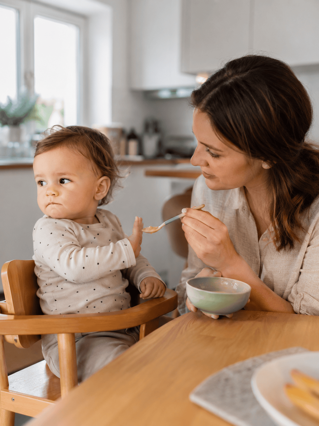 Mama karmi łyżeczką dziecko siedzące w krzesełku, dziecko odwraca głowę i odmawia jedzenia